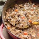 Wild rice soup in a pink pot with a spoon.