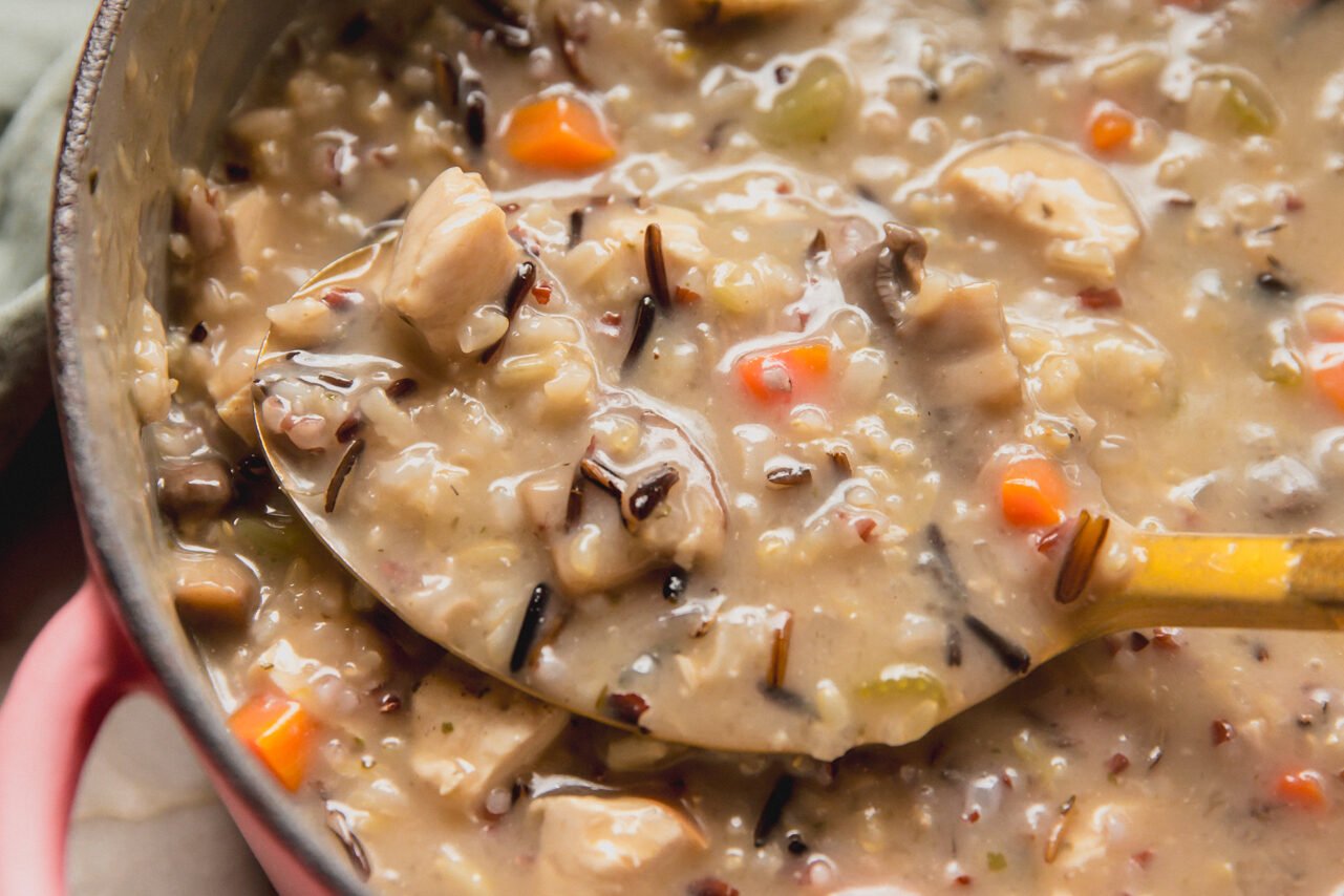 Wild rice soup in a pink pot with a spoon.