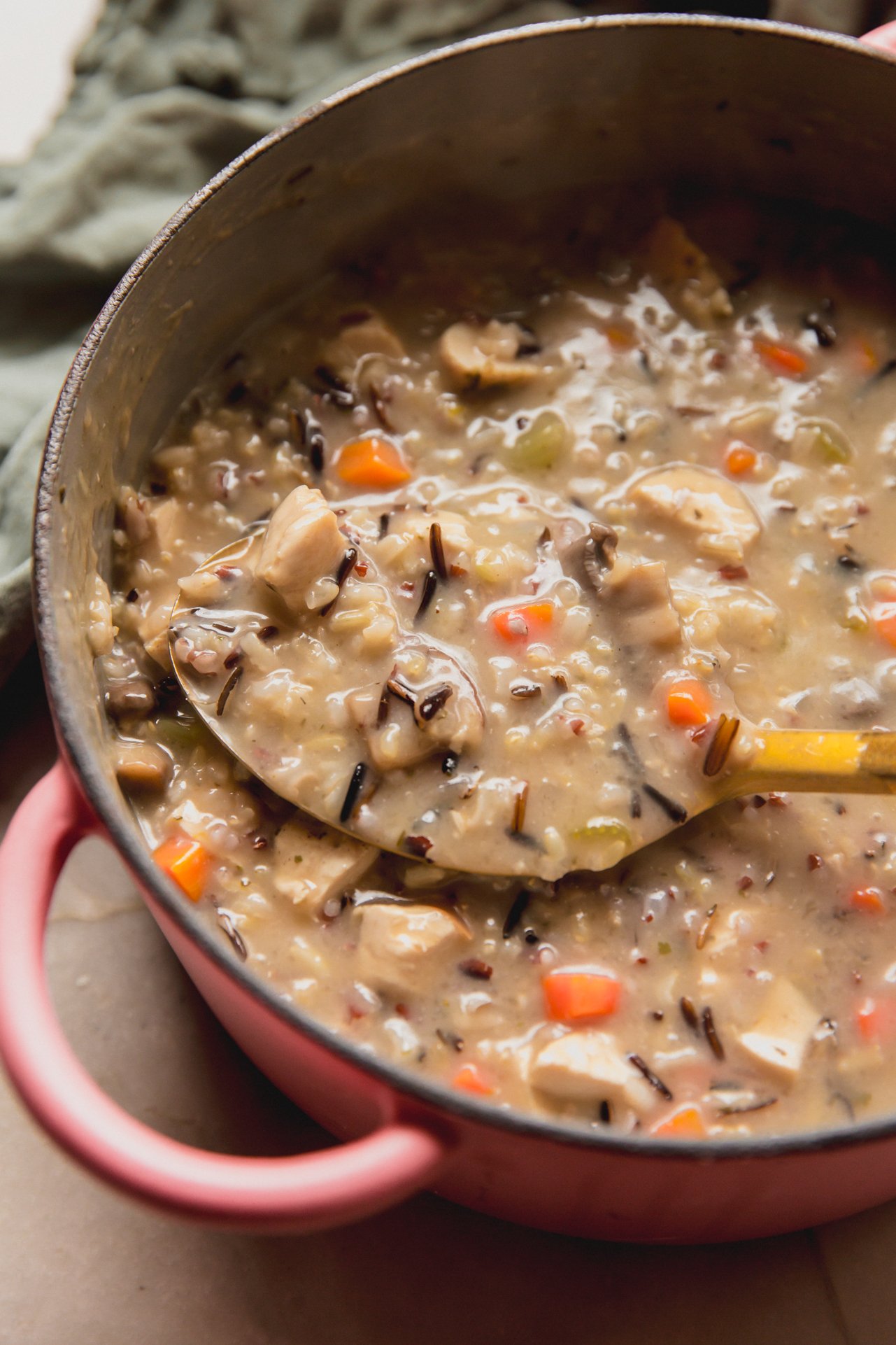 Wild rice soup in a pink pot with a spoon.