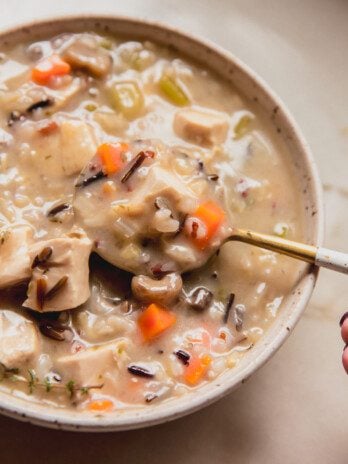 Wild rice soup with carrots, mushrooms and herbs in a bowl with a spoon.