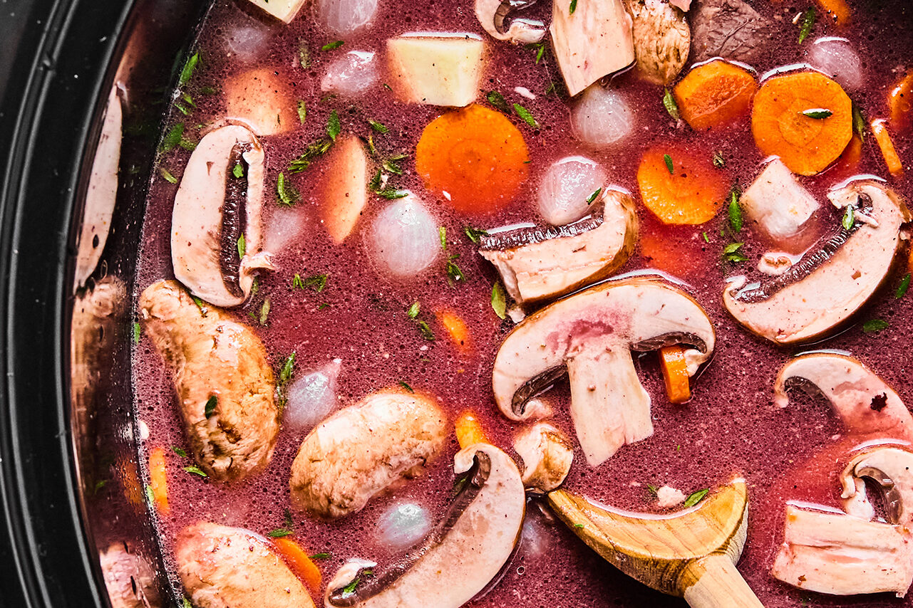 A slow cooker filled with vegetables, broth, and wine before cooking.