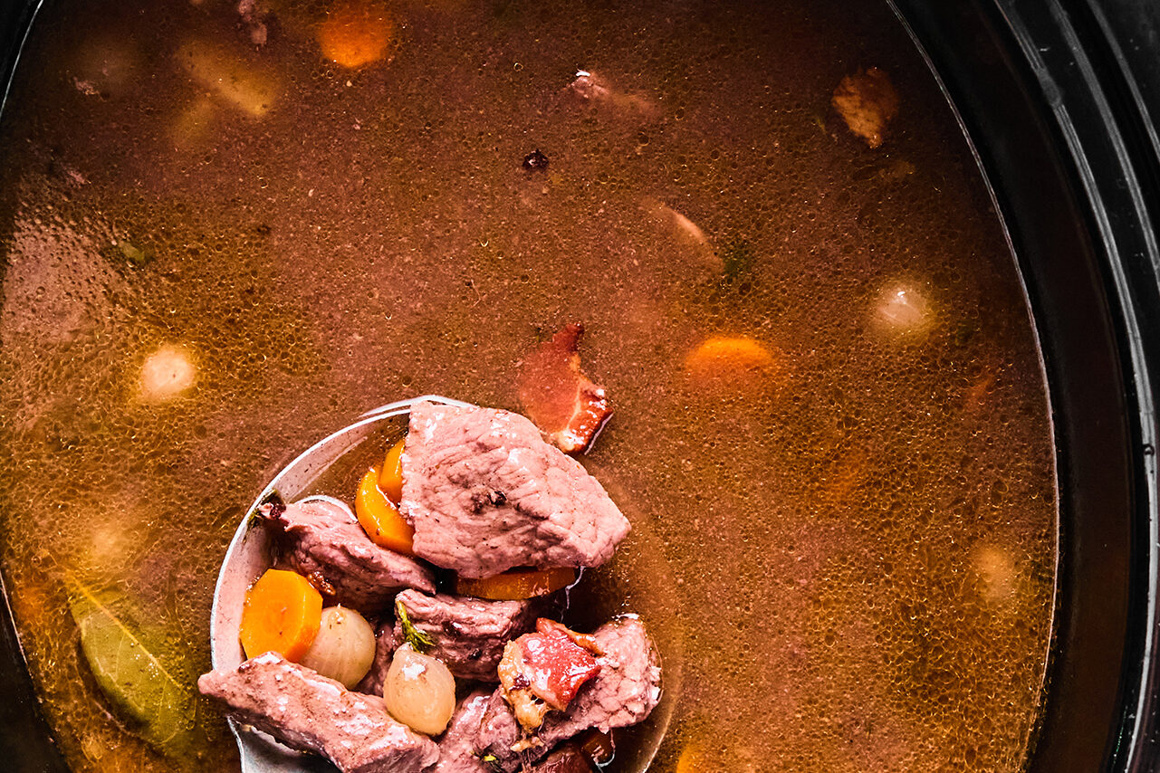A laddle scooping a serving of beef bourguignon out after it has finished cooking.
