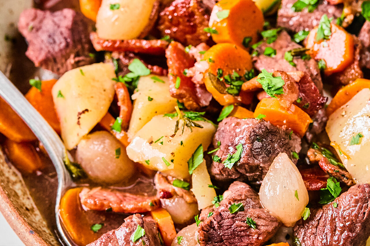 Slow cooker beef bourguignon in a large bowl with a spoon.