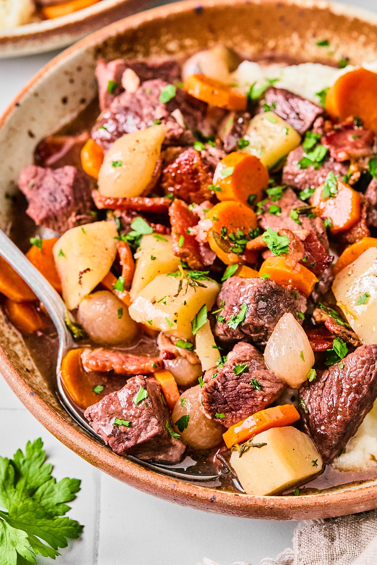 Slow cooker beef bourguignon in a large bowl with a spoon.