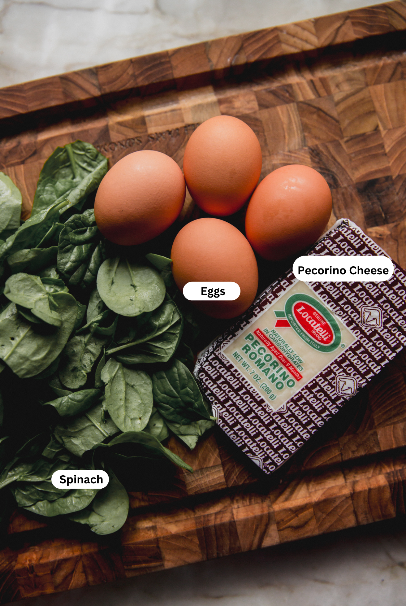 The eggs, spinach, and pecorino cheese needed to make teh stracciatella soup laid out on a wood cutting board.