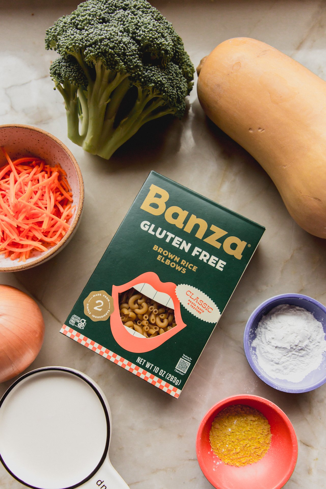 Broccoli cheese noodle soup ingredients on a marble counter top.