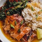 A bowl of sauteed vegetables, sliced chicken thighs, rice, lime and green onion in a ginger broth.