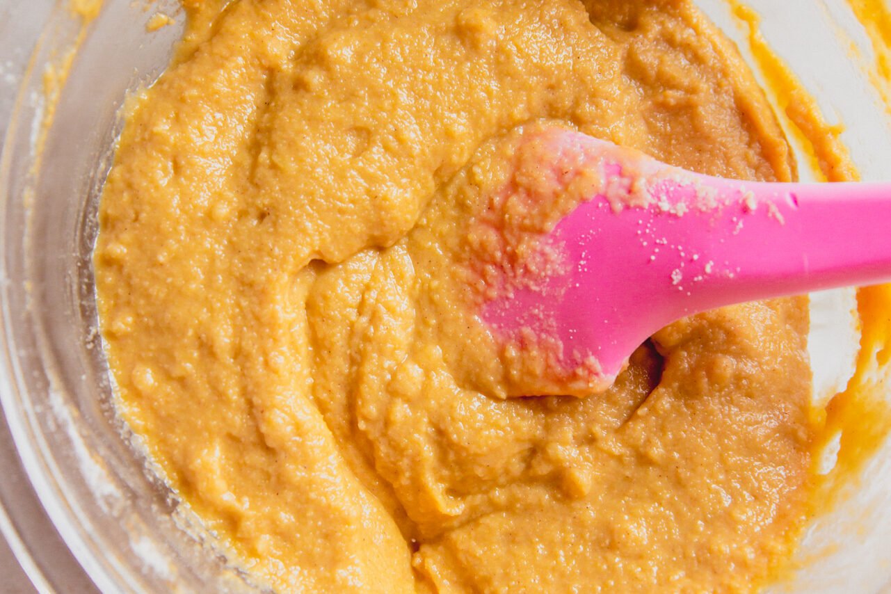 A glass bowl filled with cinnamon roll cake batter and a pink spatula.