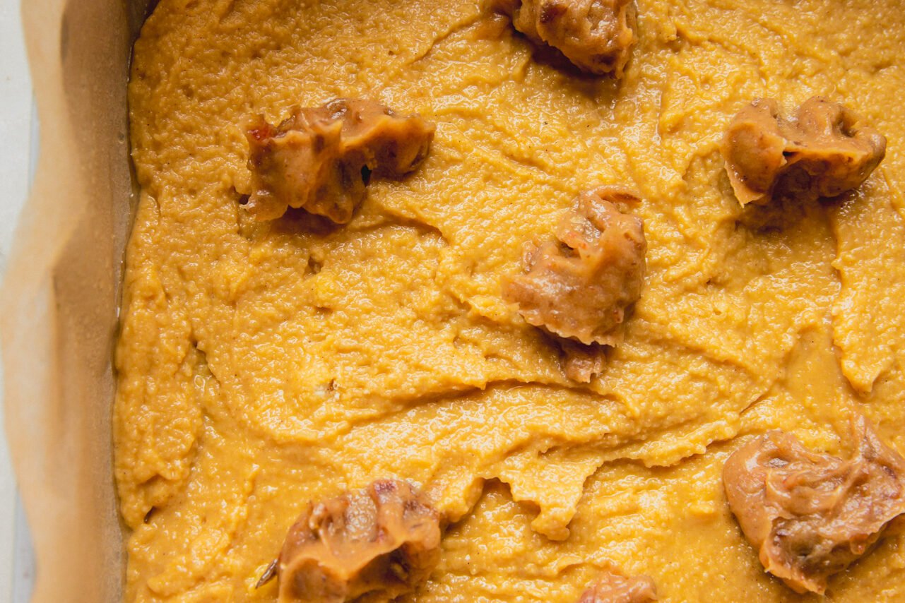 A baking dish with the cinnamon roll cake batter spread across it with small bits of the date mixture on top.