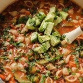 Conchitas con carne soup in a large white dutch oven, topped with avocado and cilantro.
