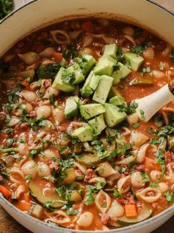 Conchitas con carne soup in a large white dutch oven, topped with avocado and cilantro.