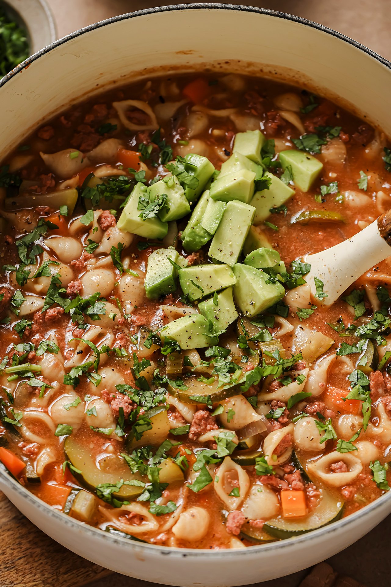 Conchitas con carne soup in a large white dutch oven, topped with avocado and cilantro.