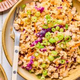 Egg roll in a bowl in a white dish with a fork topped with green onion.