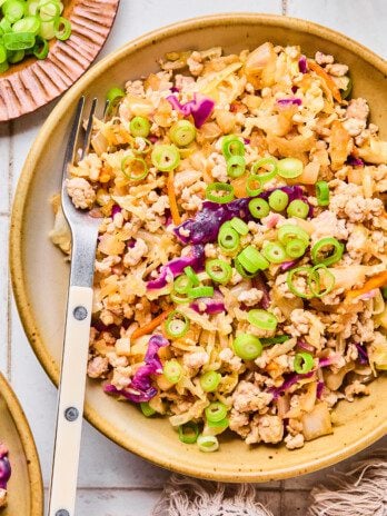Egg roll in a bowl in a white dish with a fork topped with green onion.