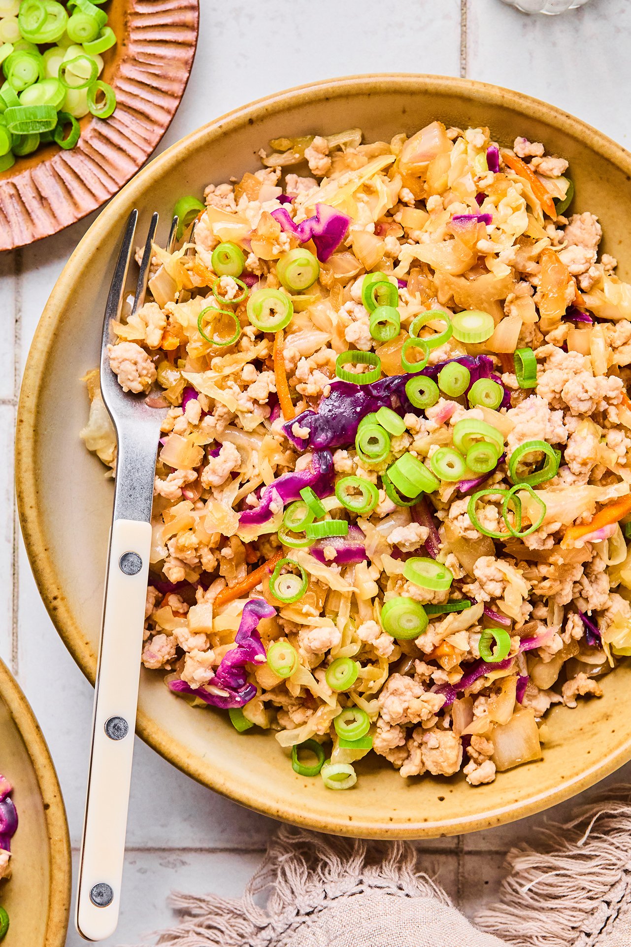 A bowl filled with egg roll in a bowl topped with green onions with a fork laid into the bowl.