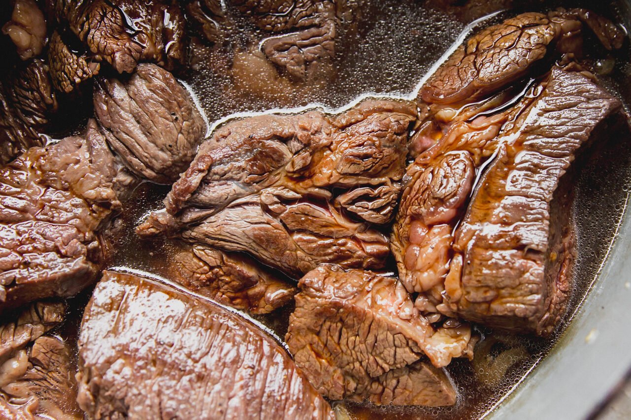 Chuck roast pieces cooked with sliced onion in liquid in a Dutch oven.