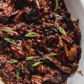 Ginger chuck roast shredded and fully cooked in a large glass dish, topped off with green onion.