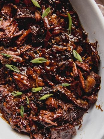 Ginger chuck roast shredded and fully cooked in a large glass dish, topped off with green onion.