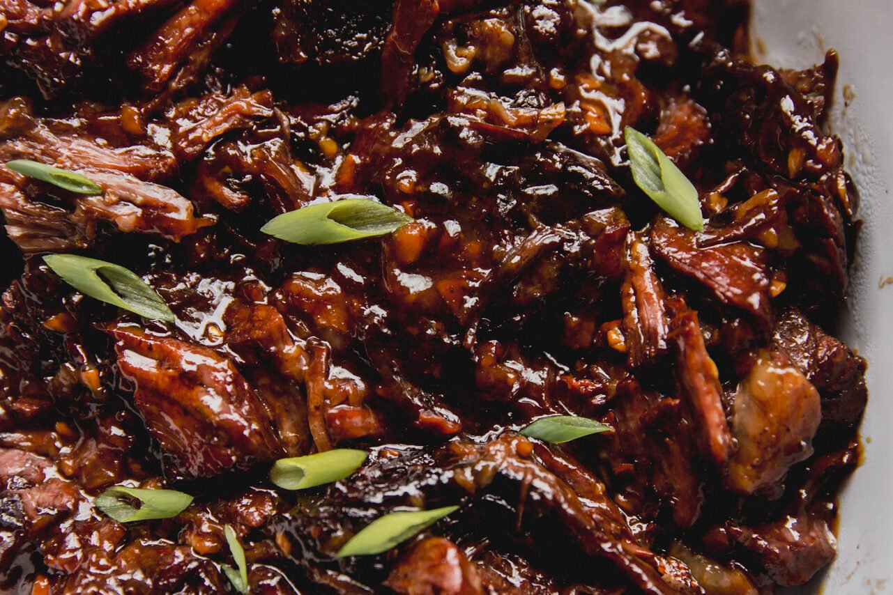 Ginger chuck roast shredded and fully cooked in a large glass dish, topped off with green onion.