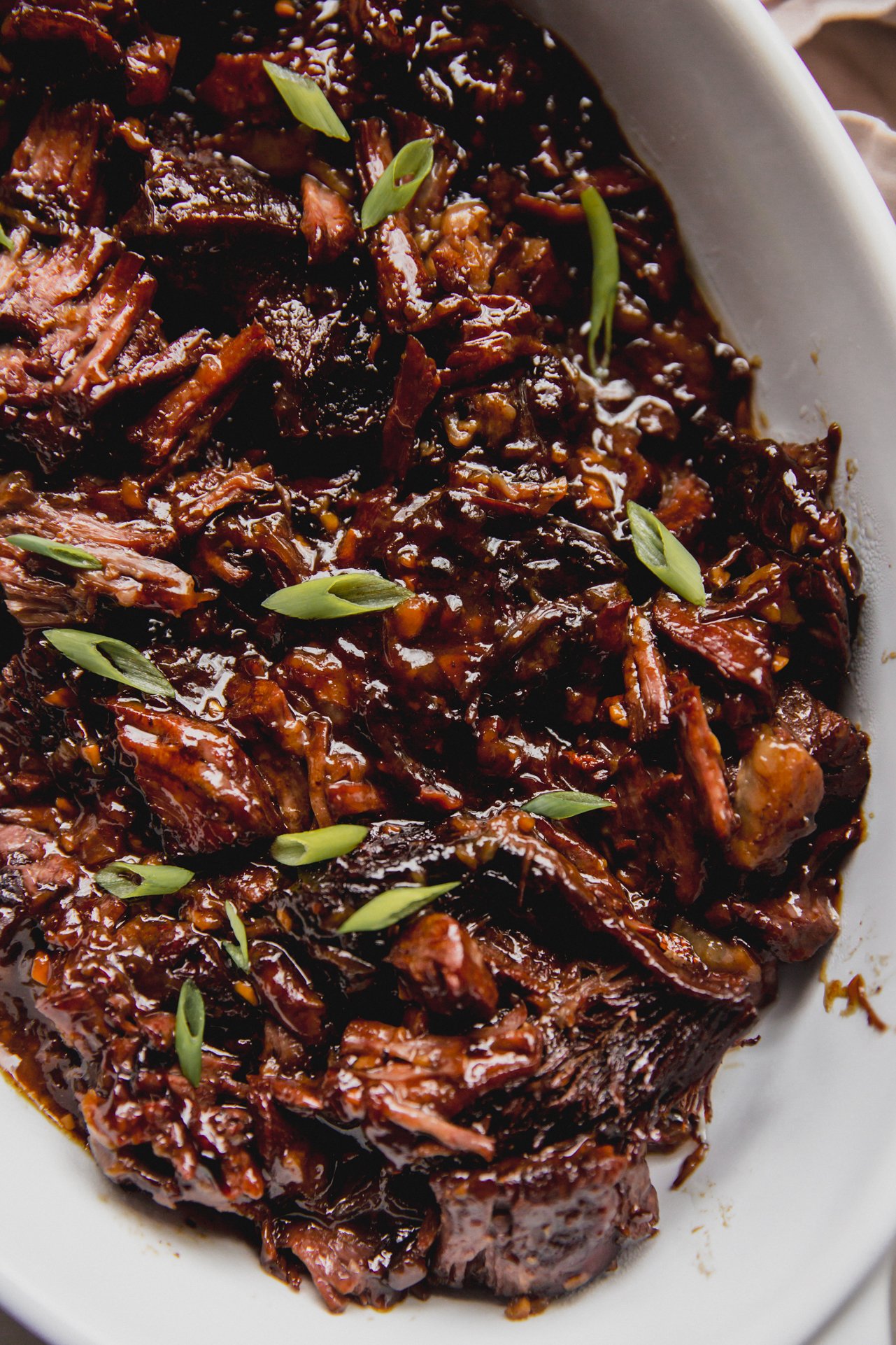 Ginger chuck roast shredded and fully cooked in a large glass dish, topped off with green onion.