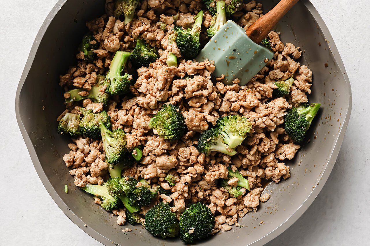 Ground chicken and broccoli fully cooked in a pan with a spatula.