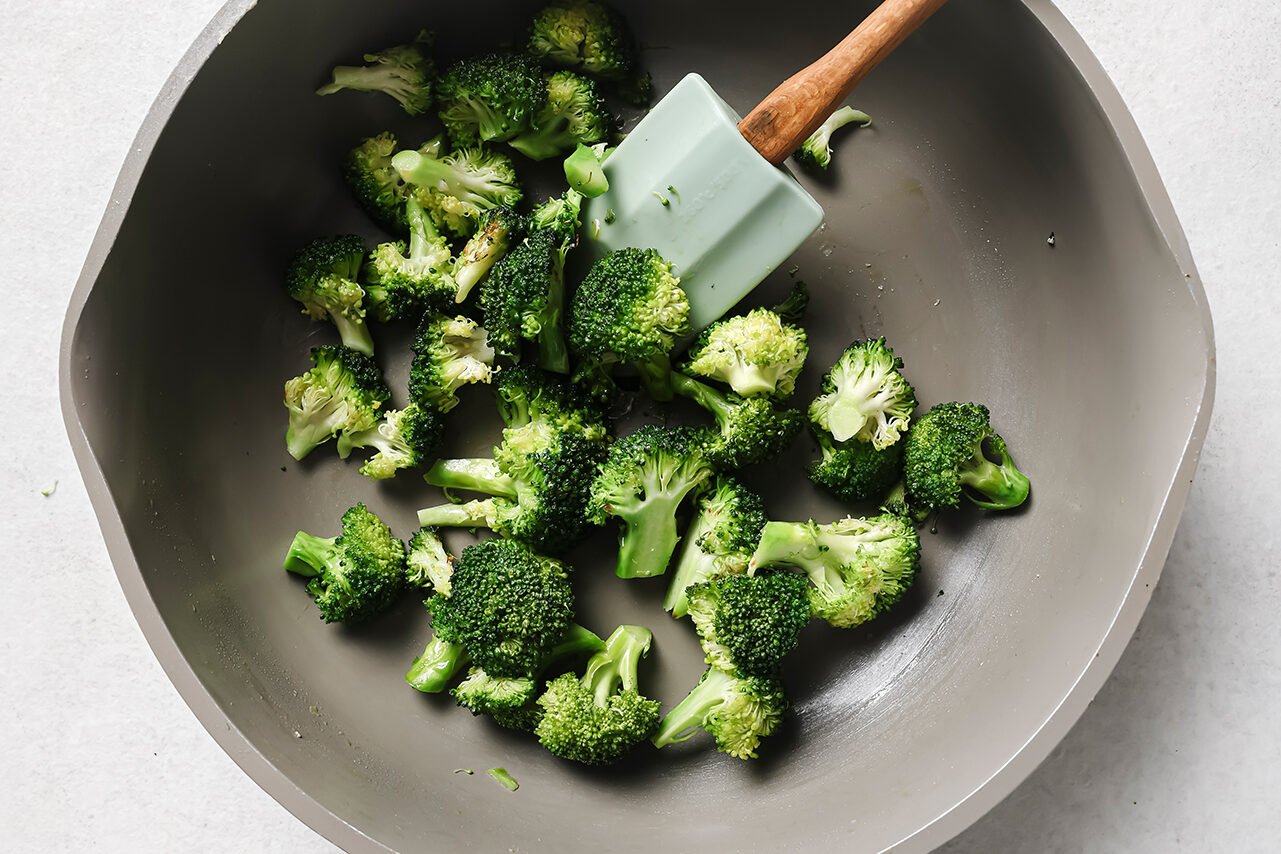 Broccoli florets sautéed in a pan.