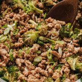 Ground chicken and broccoli in a green pan with a wooden spoon.