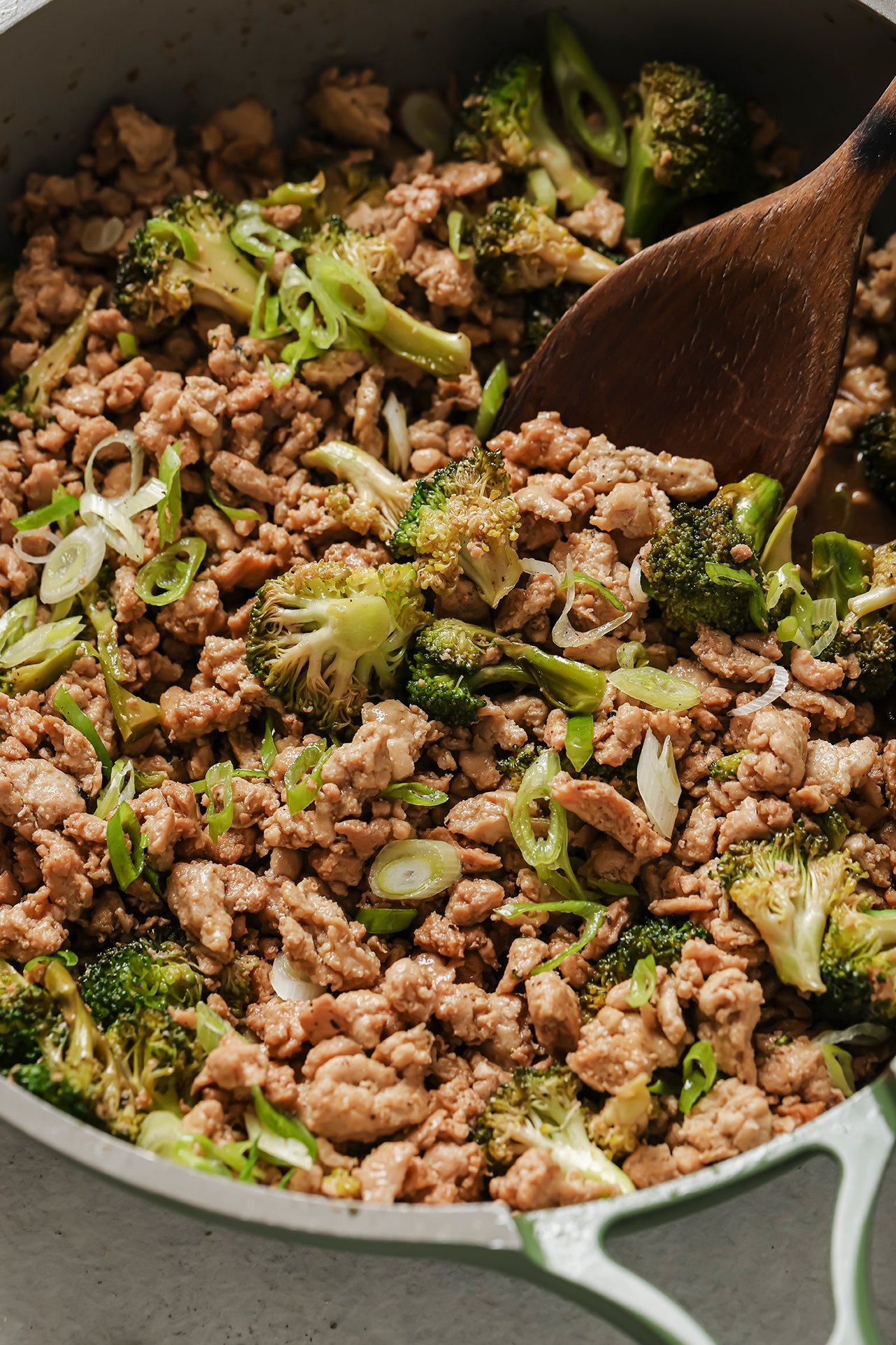 Ground chicken and broccoli in a green pan with a wooden spoon.