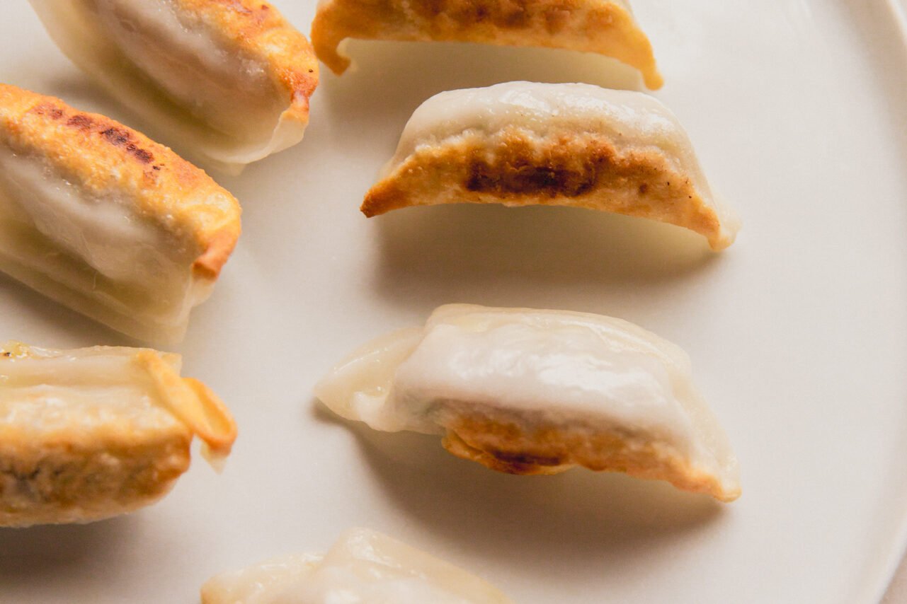A white plate with 6 potstickers after cooking set aside.