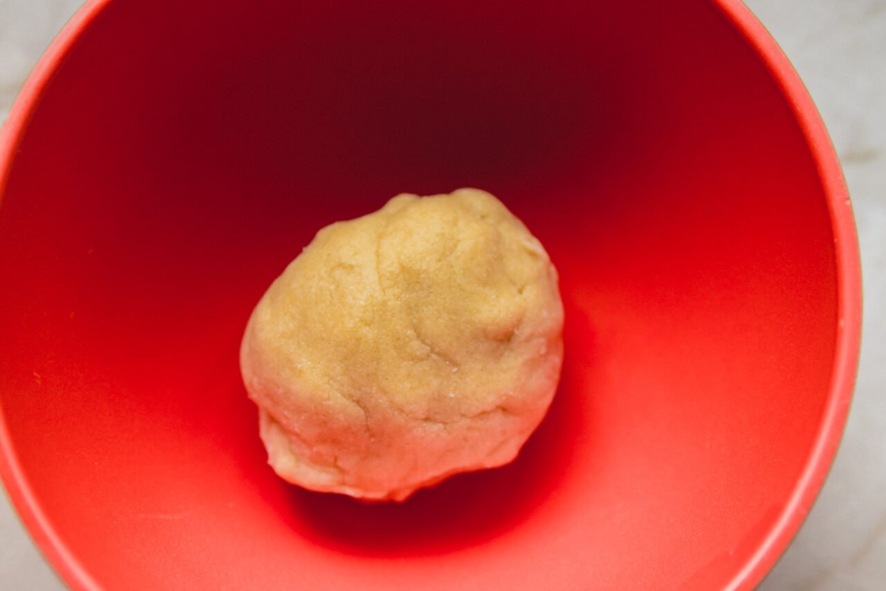 A red bowl with the slice and bake cookie dough in it in a ball.