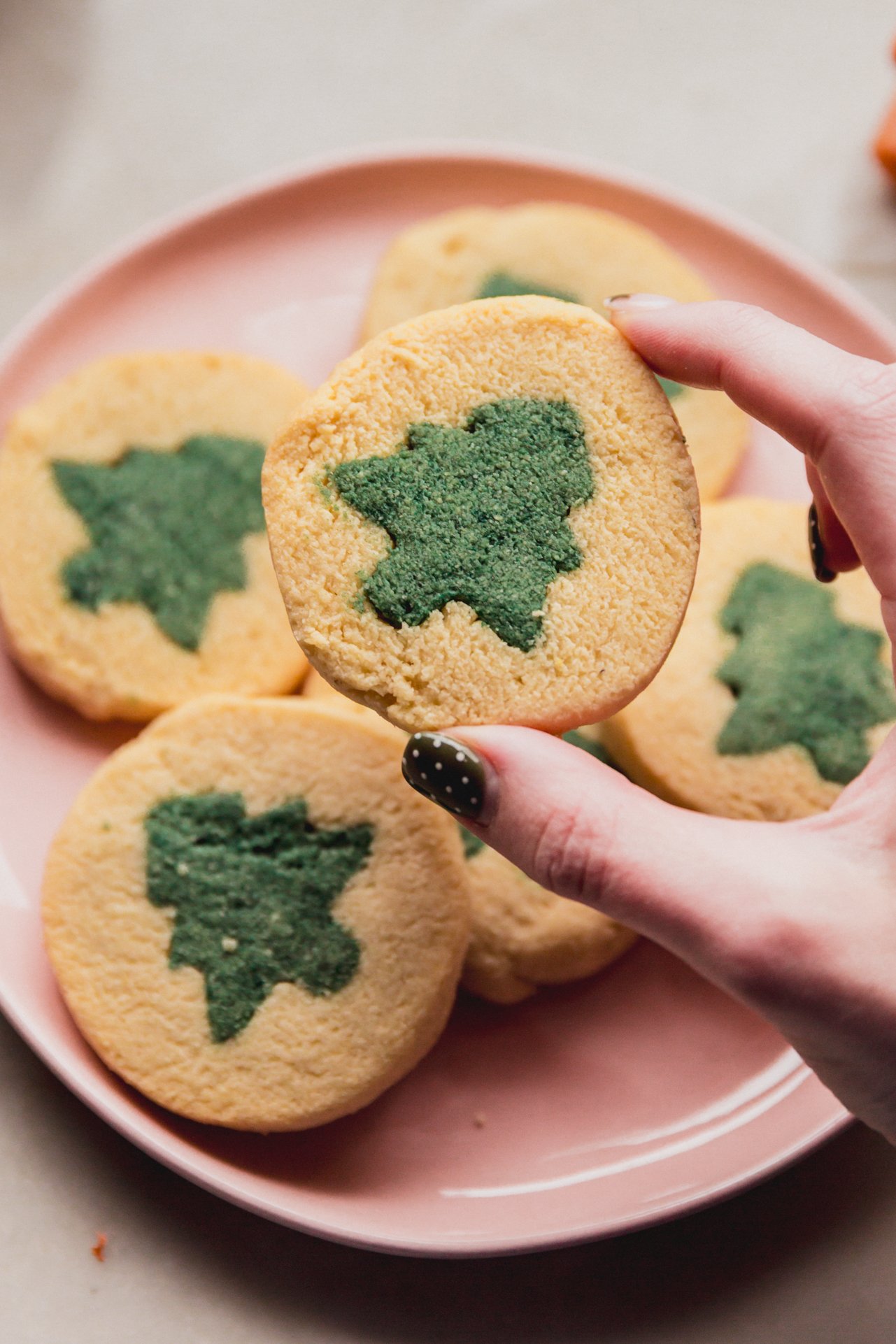 A pink plate of slice and bake cookies with a green christmas tree design.