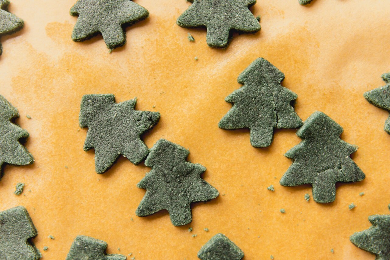 A piece of parchment paper with green cut out christmas trees of dough.