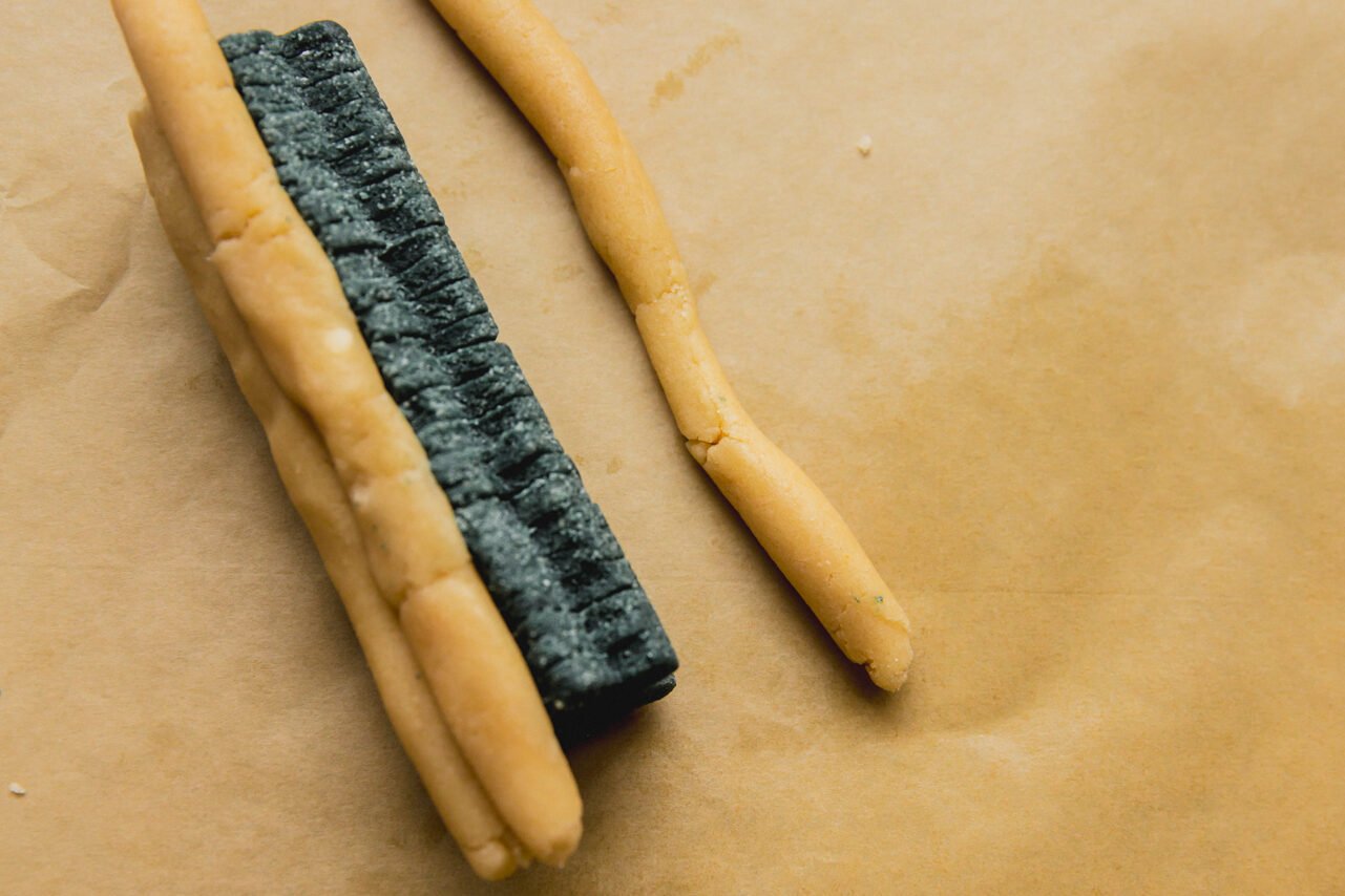 A log of green dough cut into christmas trees with three long rolls of uncolored dough pressed against it.