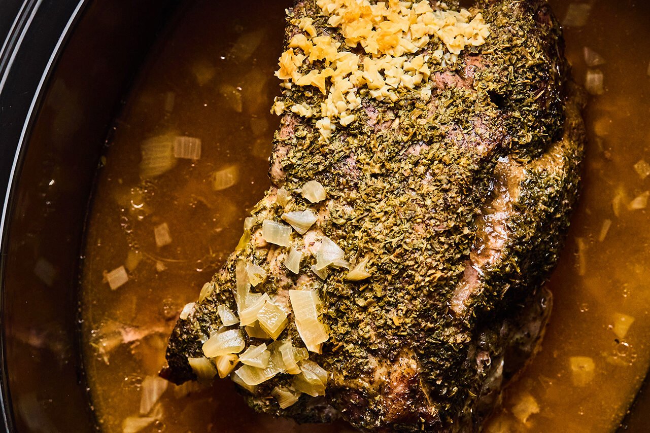 Cooked pork shoulder in a slow cooker with the cooking liquid.