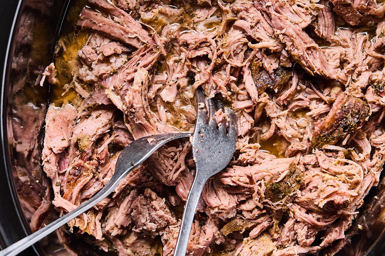 Shredded carnitas in a slow cooker with two forks.