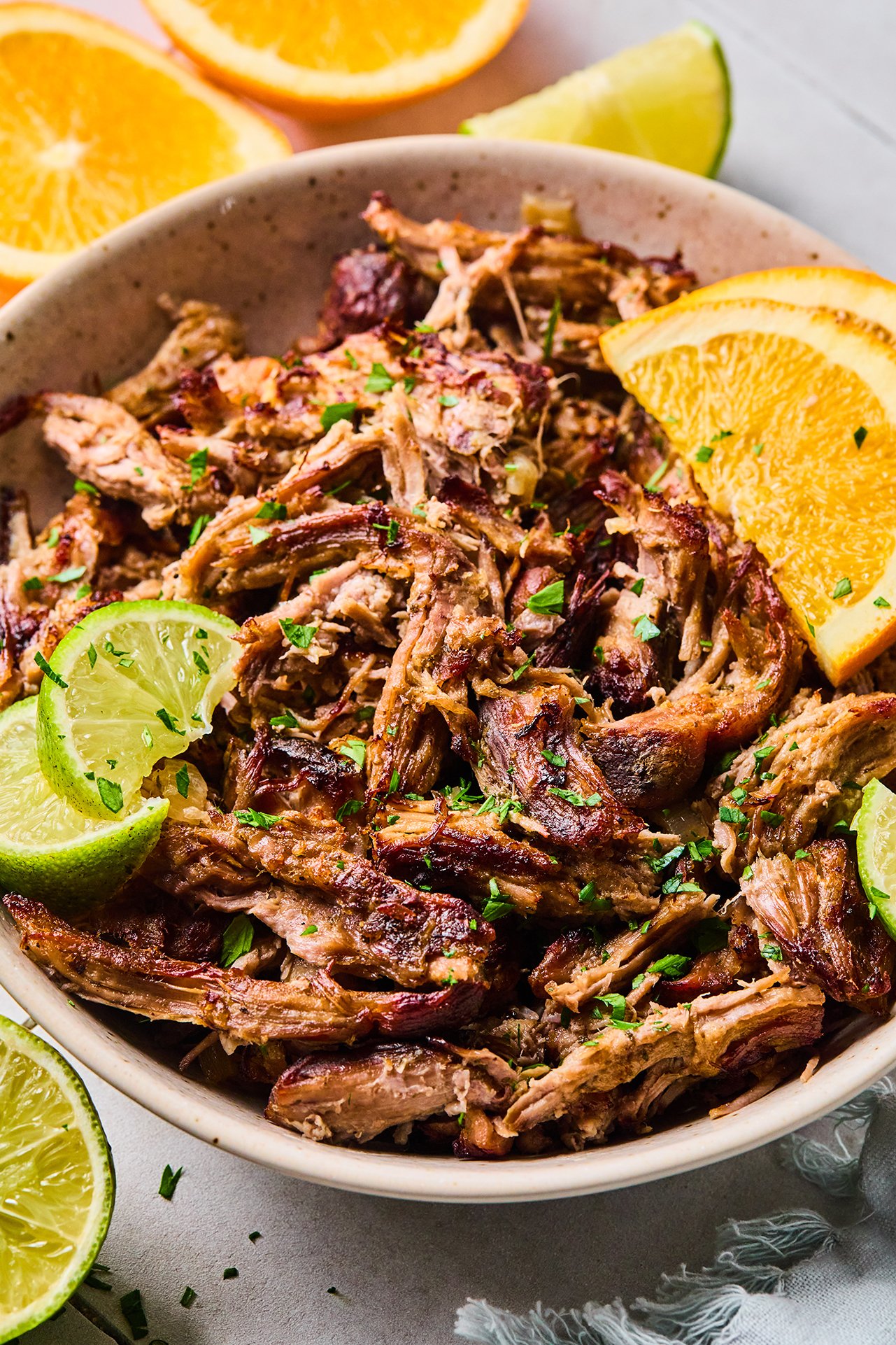 Slow cooker carnitas shredded in a bowl and topped with sliced lime, orange and chopped cilantro.