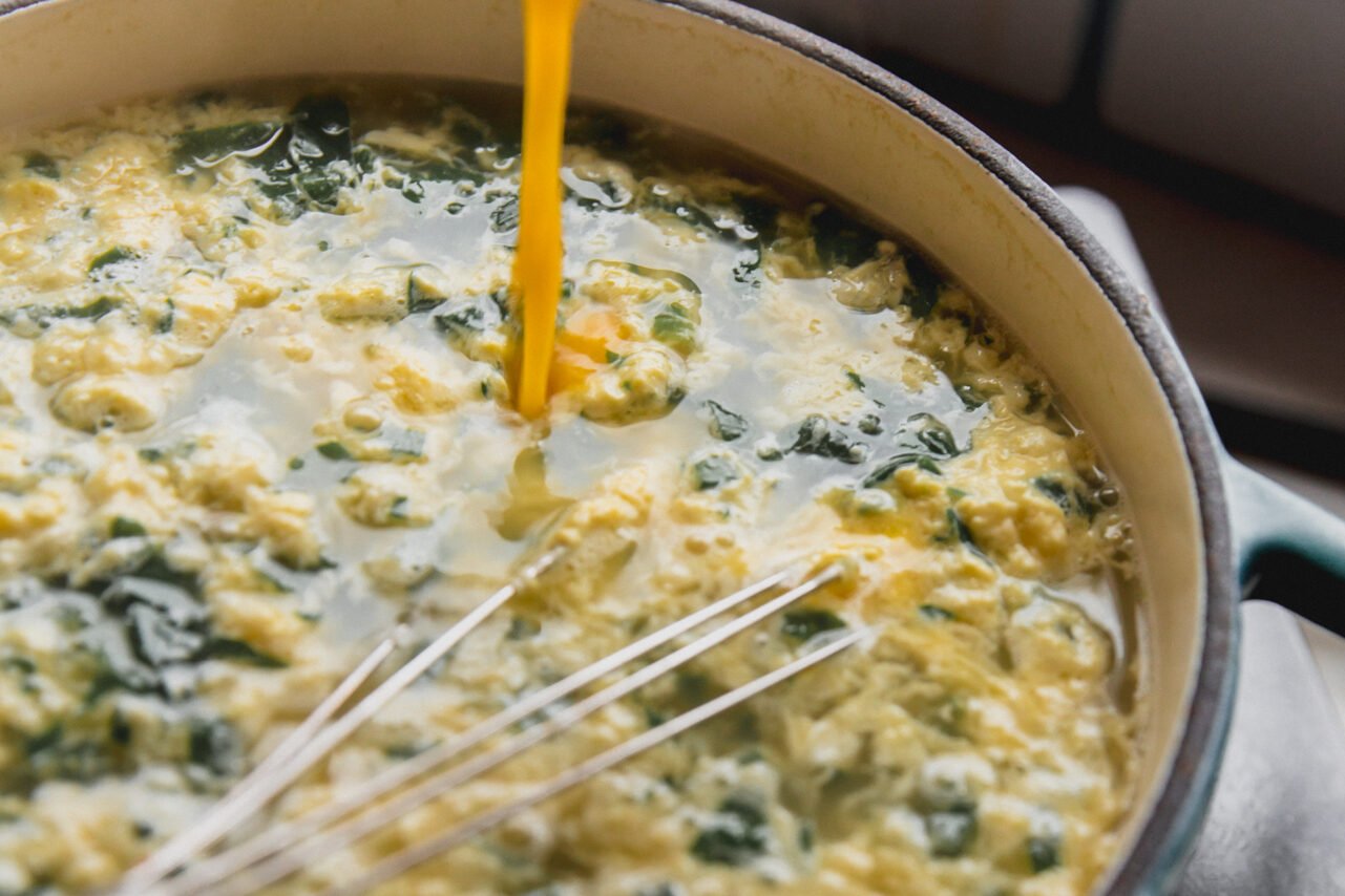 The egg mixture streaming into a pot with the spinach and broth mixture.