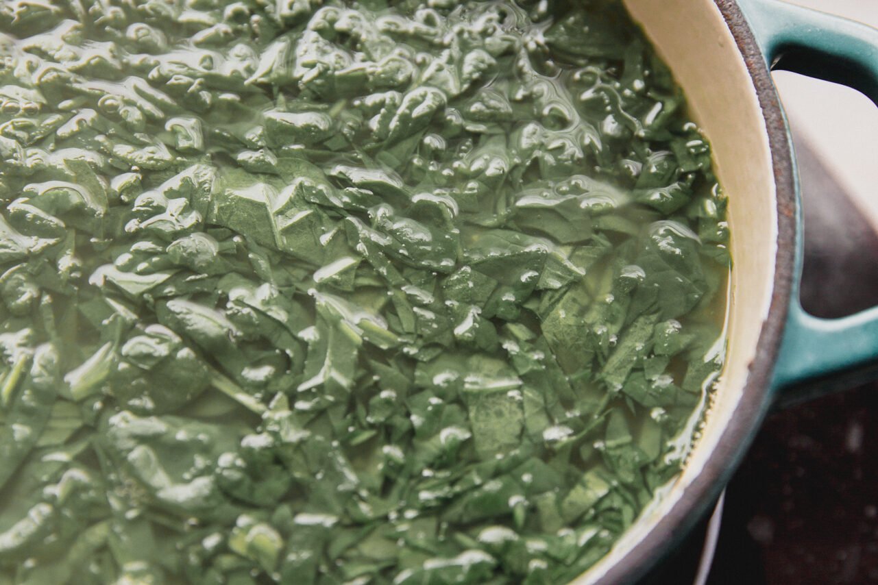 The chicken broth, lemon juice, and spinach in a pot simmering.