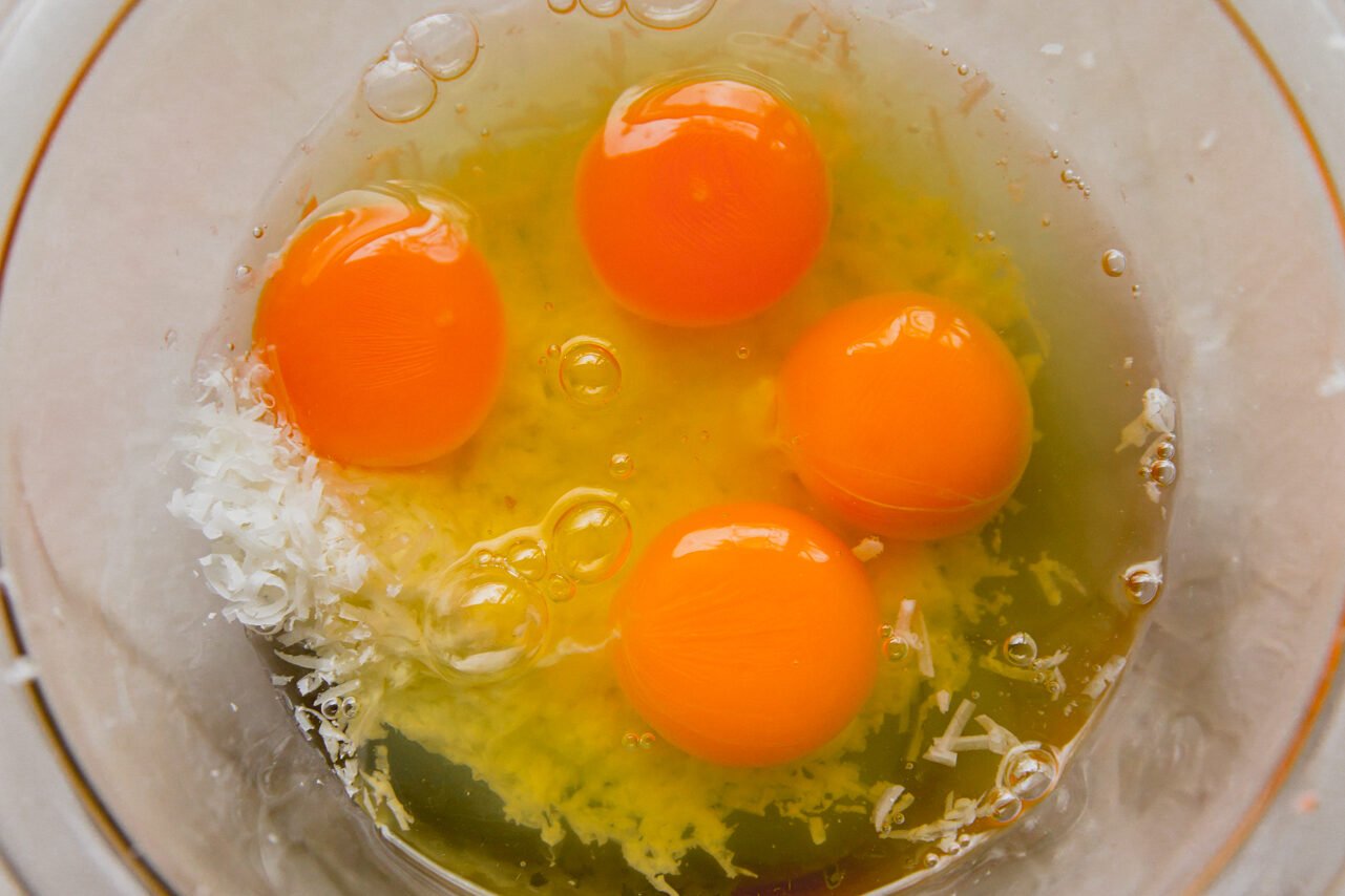A glass bowl with four eggs and cheese in it before mixing.