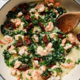 Tuscan garlic shrimp in a large white enamel pan with a wooden spoon.