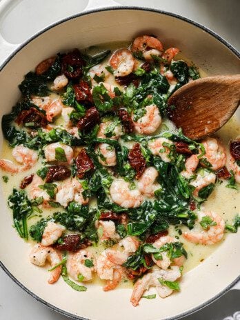Tuscan garlic shrimp in a large white enamel pan with a wooden spoon.