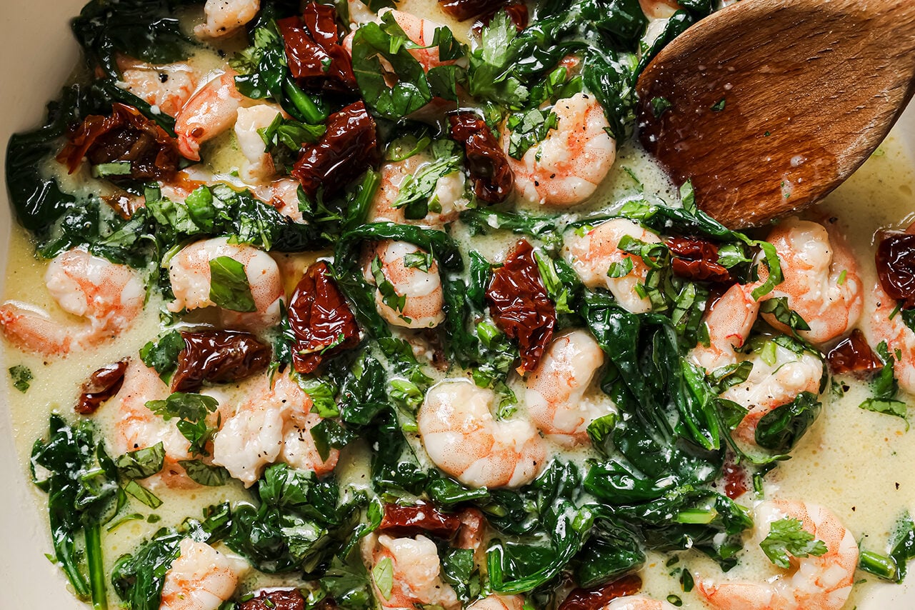 Tuscan garlic shrimp in a large white enamel pan with a wooden spoon.
