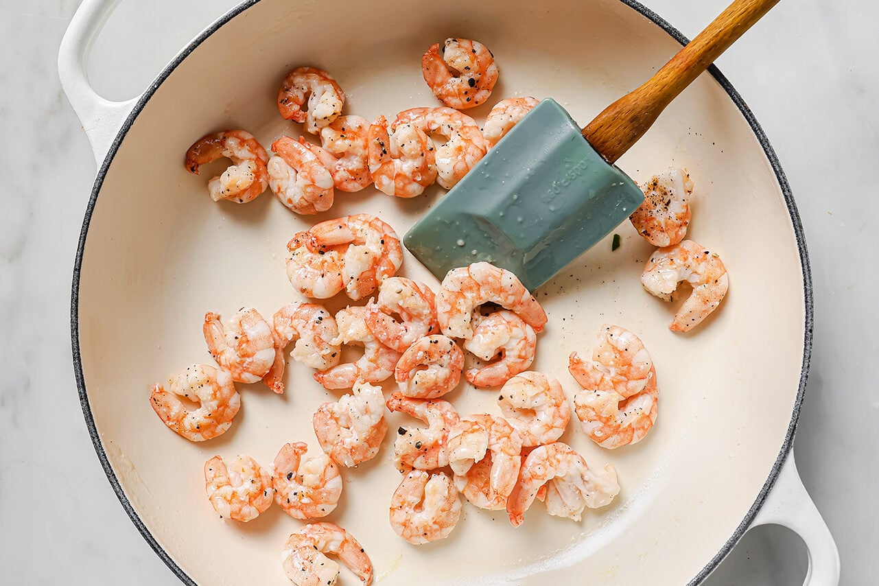 Shrimp cooking in a white skillet with a spatula turning the shrimp.