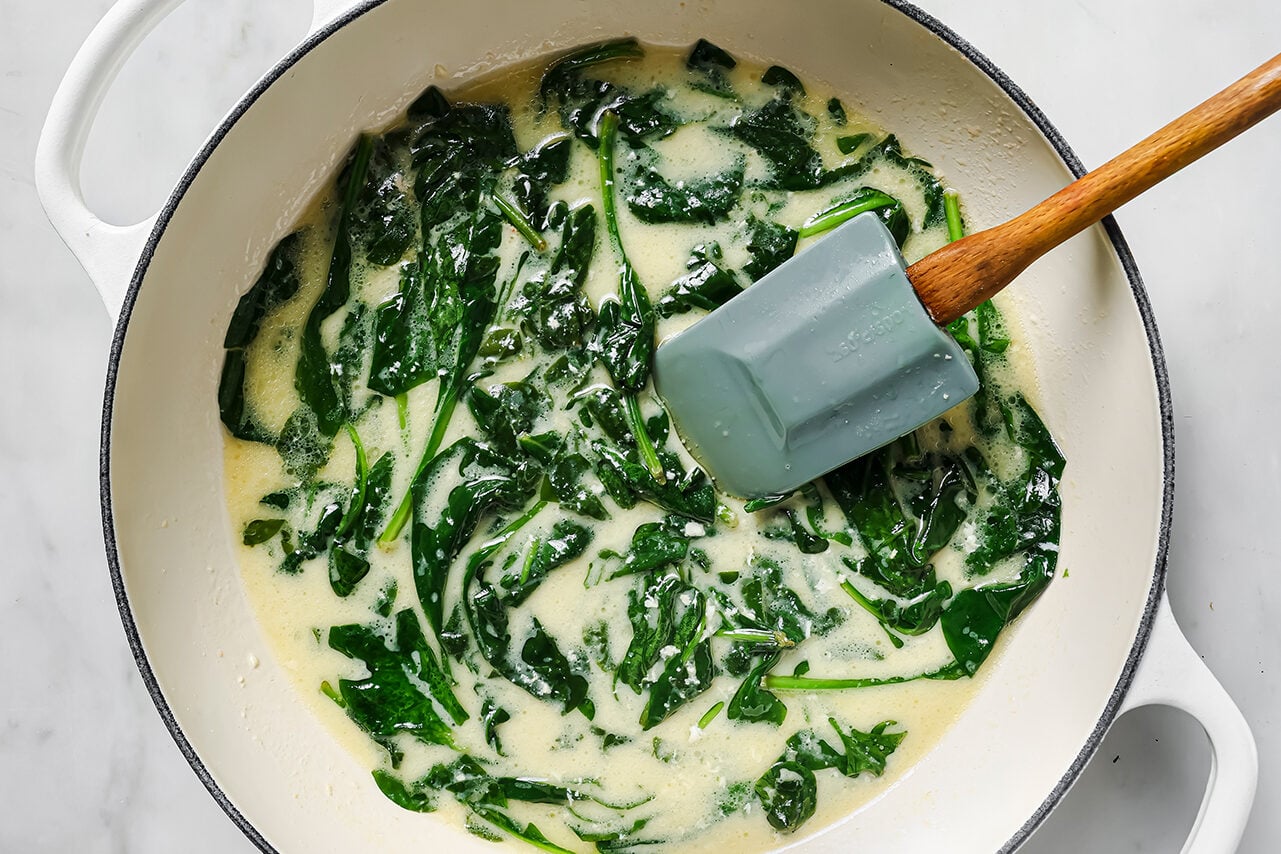 A white pan with sauted spinach and the sauce poured in it.
