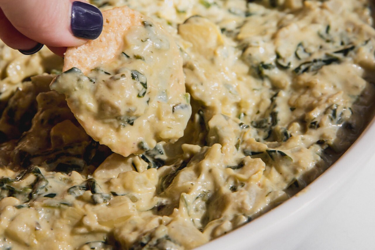 A cracker scooping some of the finished spinach and artichoke dip up
