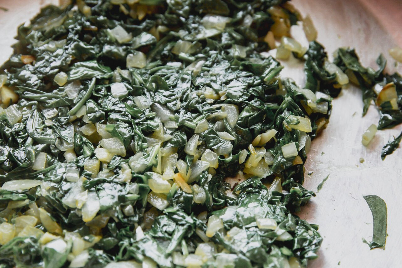 Spinach, onion, and garlic sauteeing in a pan.