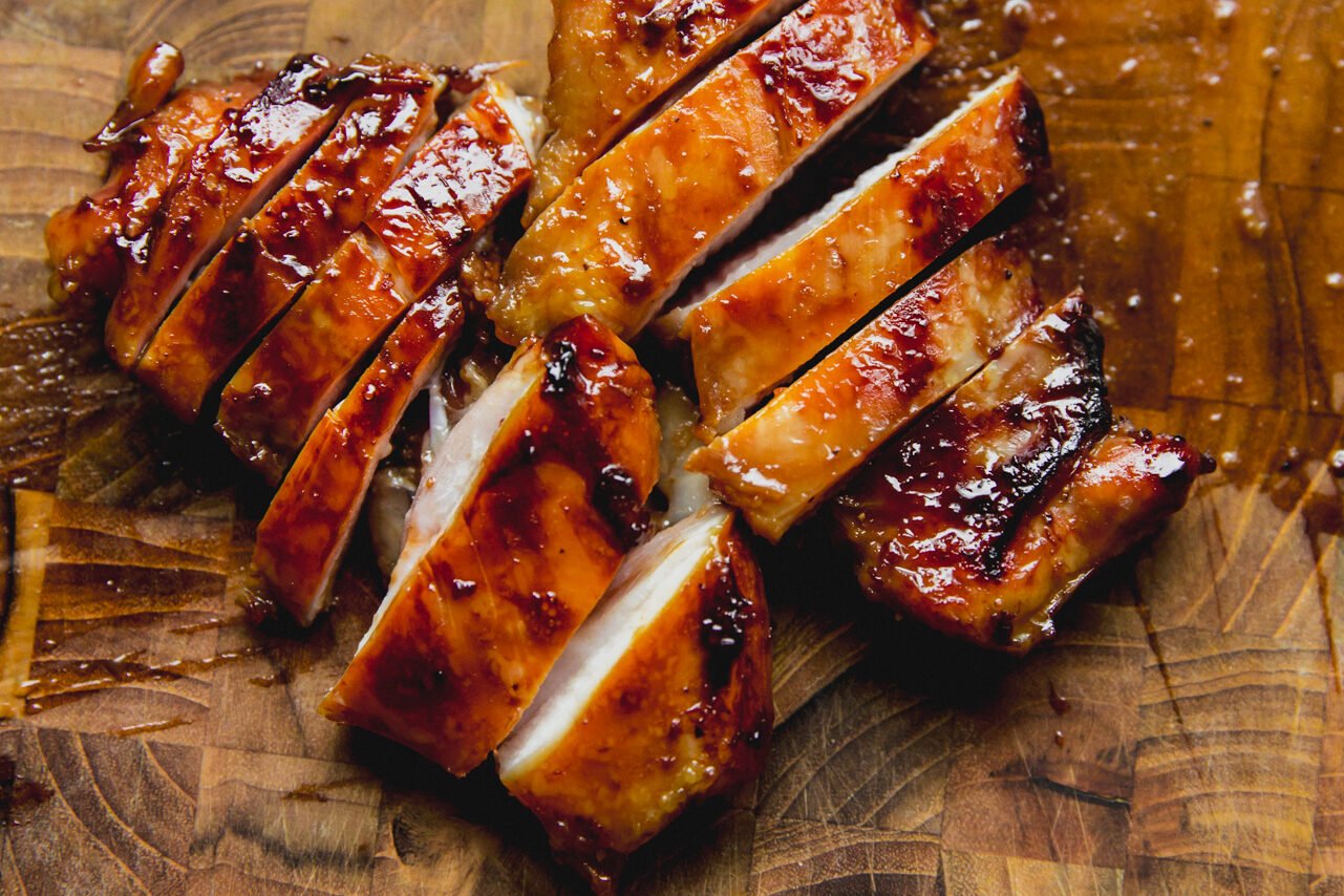 Two chicken thighs cooked and on a wooden cutting board sliced.