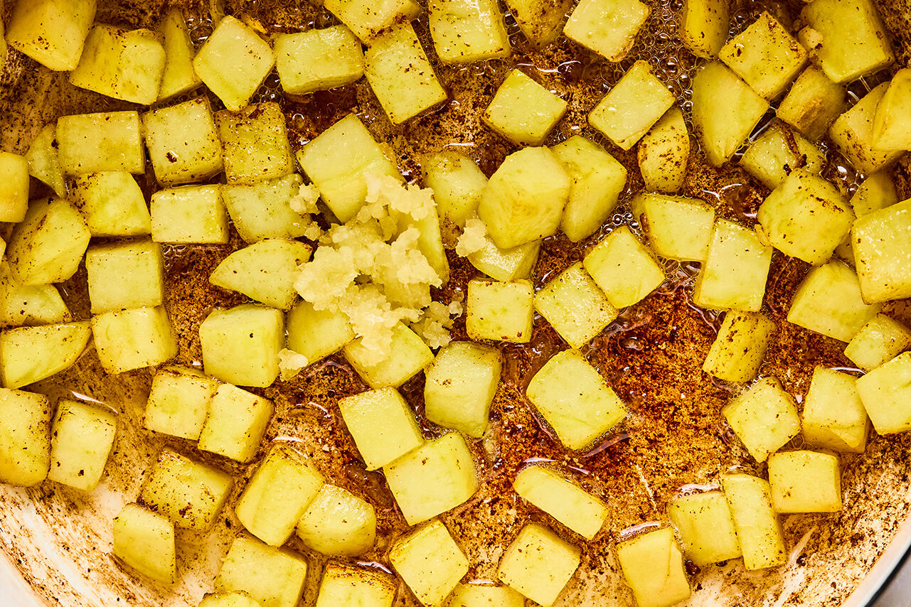 Diced sweet potato sauting in a pan with garlic added on top.