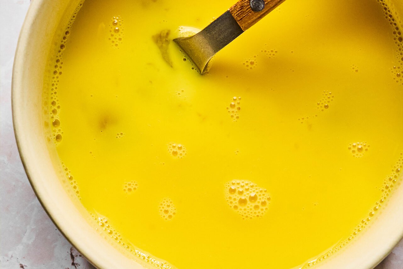 A bowl with eggs whisked with water in it and a fork in it.