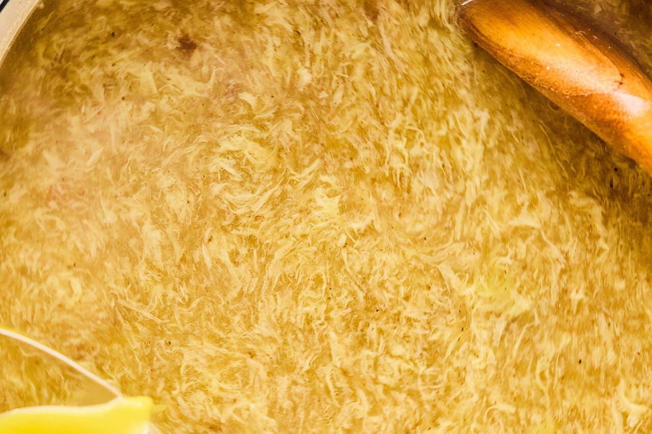 A Dutch oven filled with soup with egg in it and a wooden spoon.